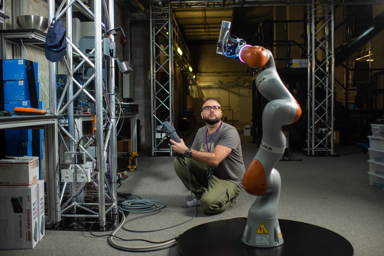 Nikolaos Giakoumidis crouching beside a KUKA LBR robotic arm he is teleoperating in the NYUAD CTP labs
