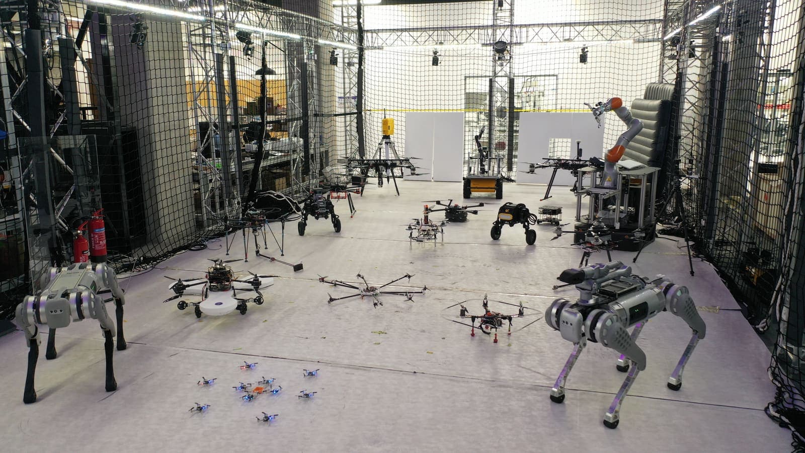 CAIR robot fleet lined up along a lab corridor: multirotor drones on the floor flanked by quadruped robots and equipment racks