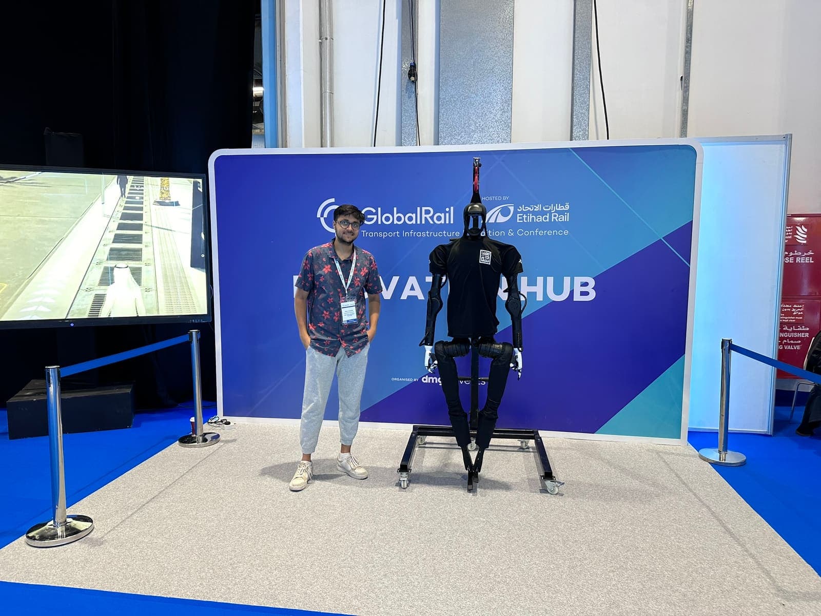 Humanoid robot standing beside a researcher in front of the Global Rail Innovation Hub backdrop