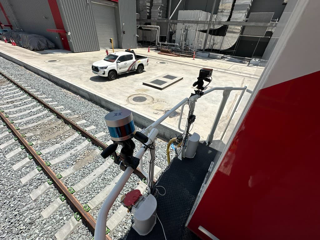 Close-up of LiDAR and camera sensors bracketed to the train rear handrail, with an Etihad Rail service vehicle beside the tracks