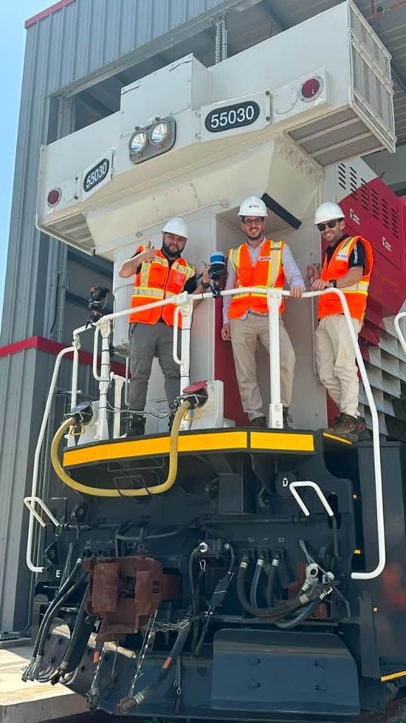 Three engineers in PPE on the rear platform of an Etihad Rail locomotive with a LiDAR and camera sensing payload mounted on the handrail