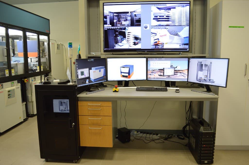 HTS control desk with four monitors, overhead camera-feed display, server rack, and emergency stop
