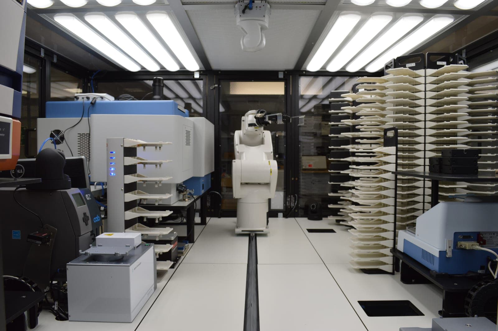 Plate-handling rail robot inside the NYUAD high-throughput screening enclosure, flanked by instrument stacks