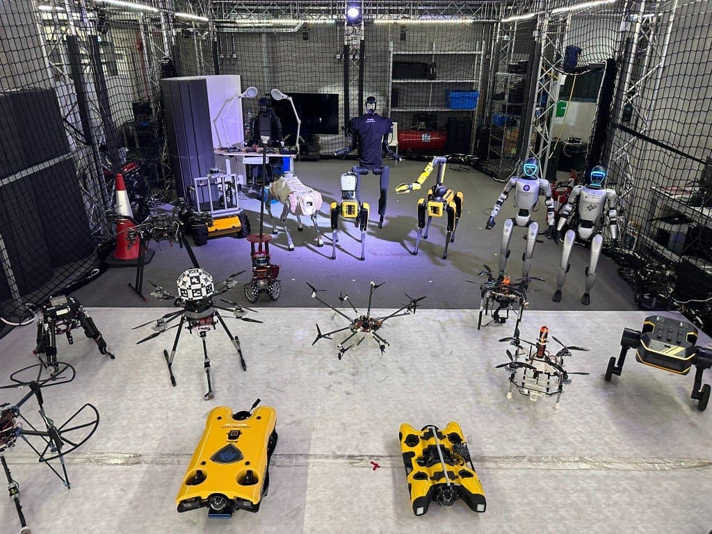 Full CAIR robot fleet staged in the Kinesis CTP arena — humanoids, Spot and other quadrupeds, multirotor drones, marine craft, and ground robots under motion-capture trusses and safety nets