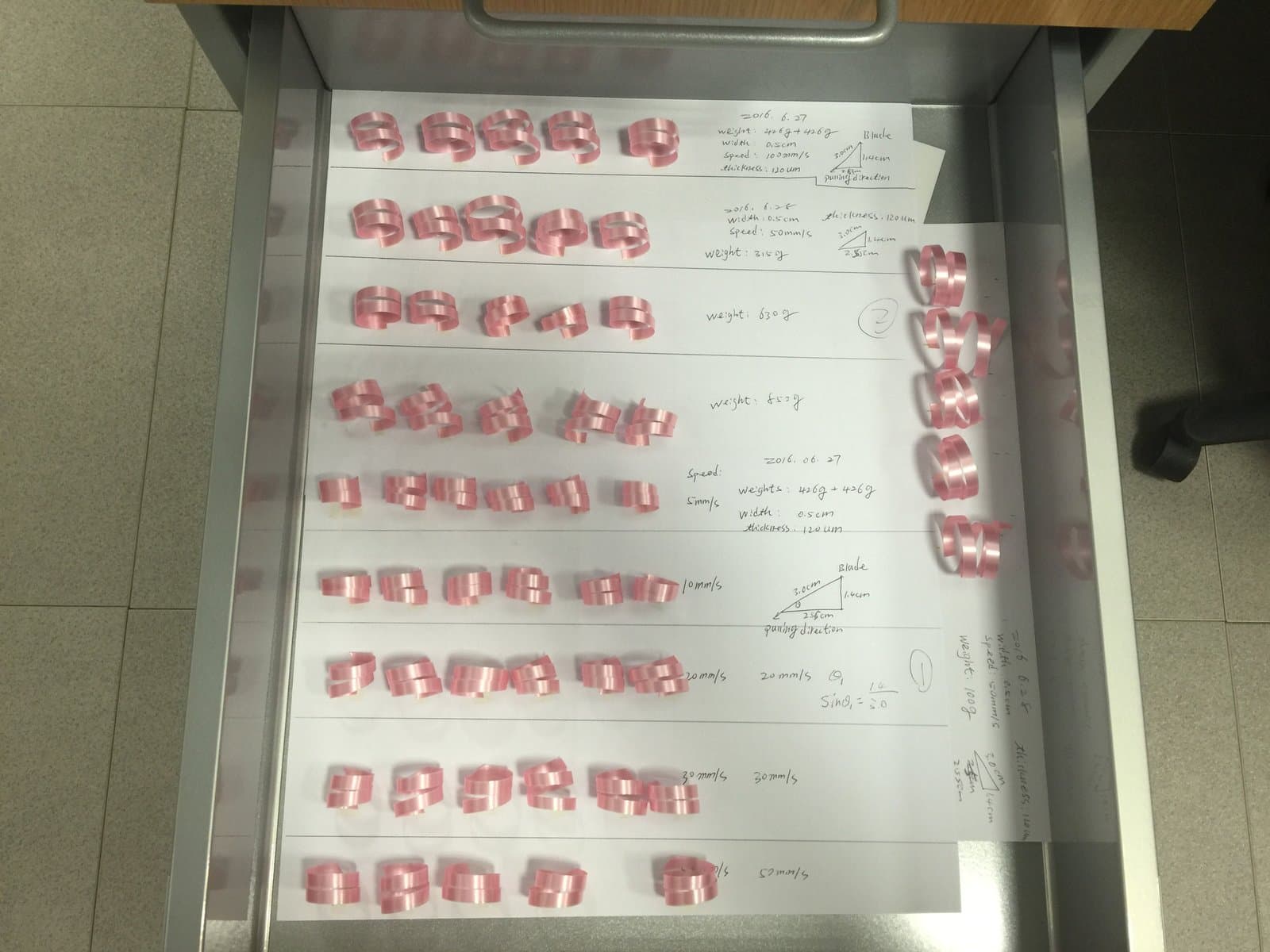 Drawer tray of pink ribbon curls with handwritten notes for weight, speed, width, and fixture geometry