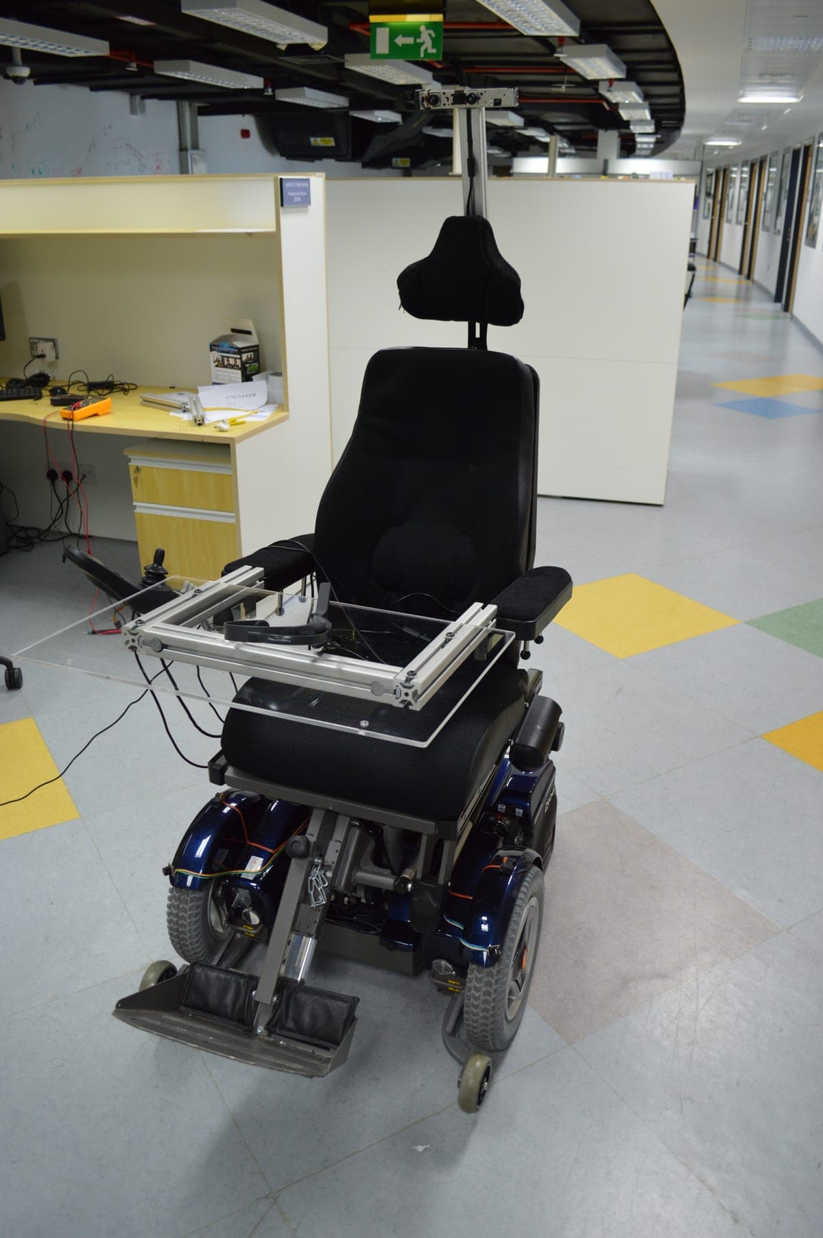 Instrumented powered wheelchair prototype with a custom sensor and gaze-tracking frame, in a lab corridor